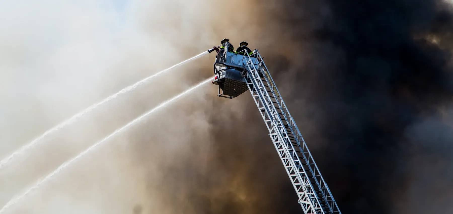 Impact investing risk, a fire crew ladder spraying water into thick smoke.