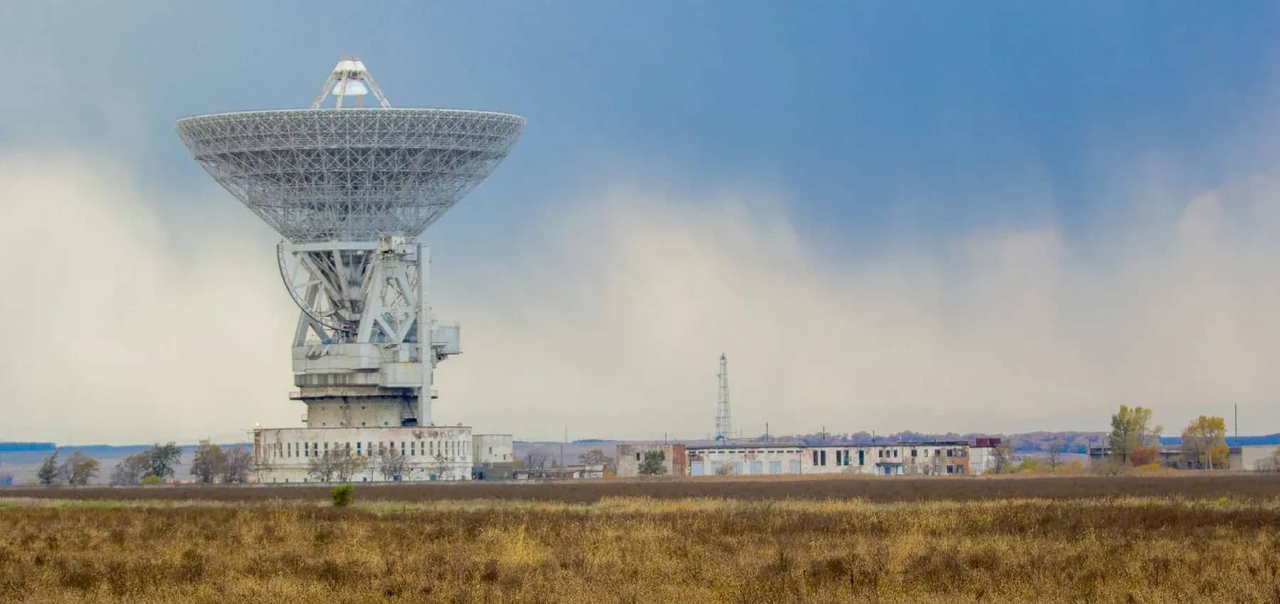 High return investments, a large radio telescope dish angled against a wide pale sky.