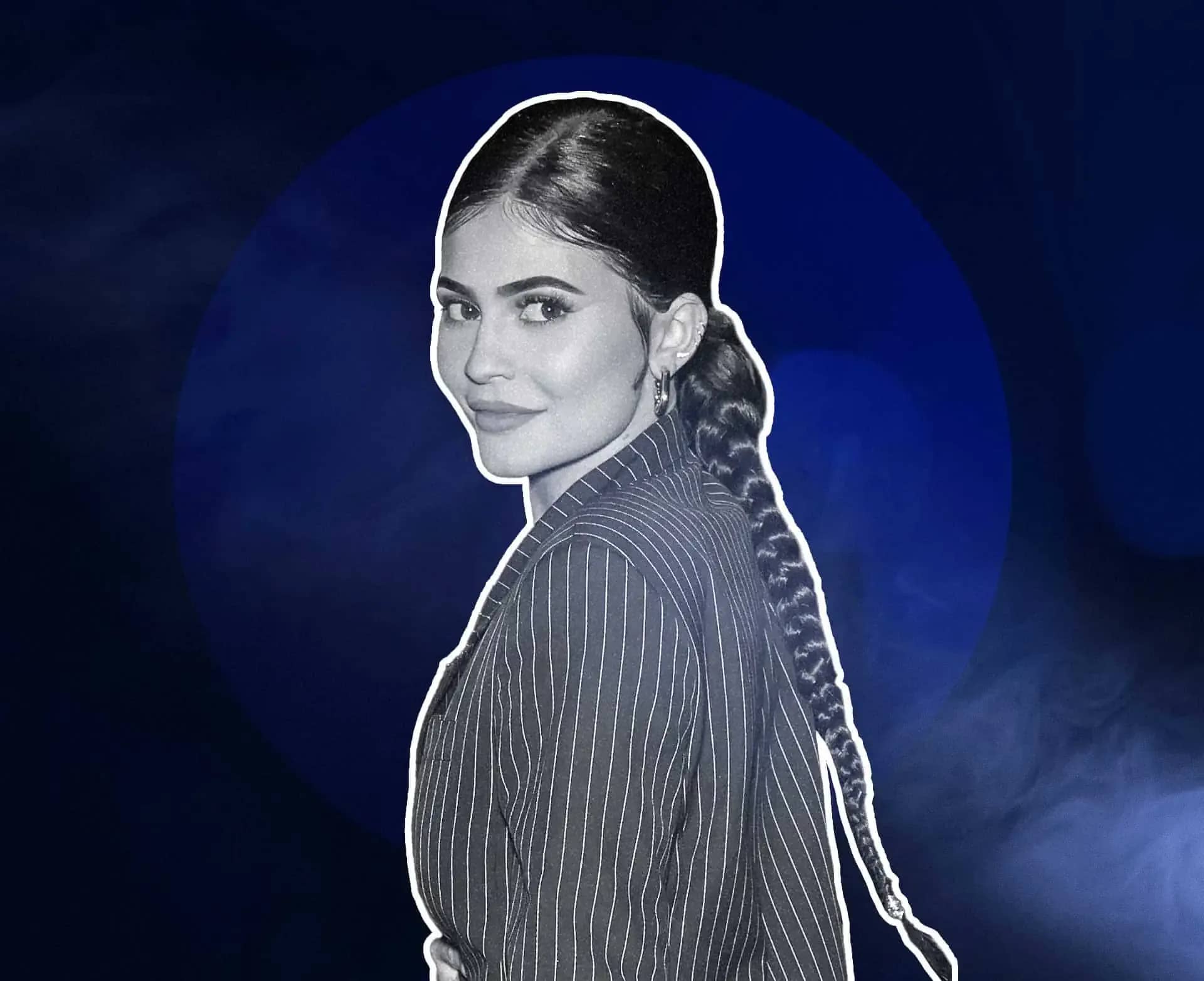 Kylie Jenner net worth, a monochrome portrait of Kylie Jenner in a pinstriped jacket against a deep blue background.