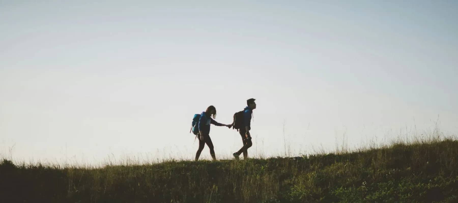 Fiduciary services technology, two hikers reaching to help each other across open ground.