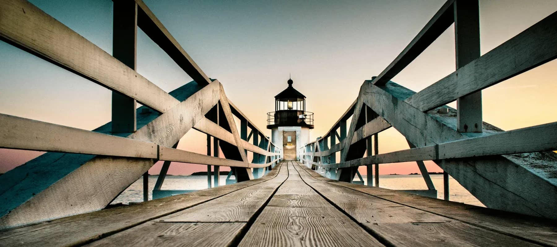 Building a brand in direct investing, a lighthouse framed by wooden trestle beams at sunset.