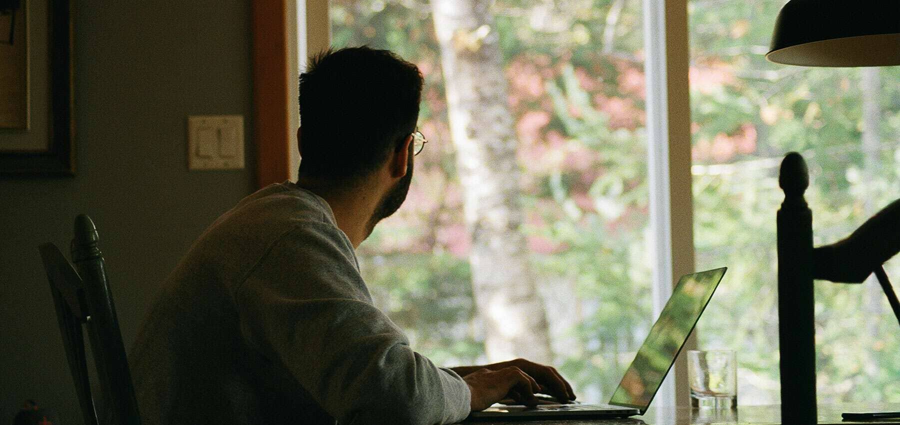 Family office strategy, a man working at a laptop beside a bright window looking onto greenery.