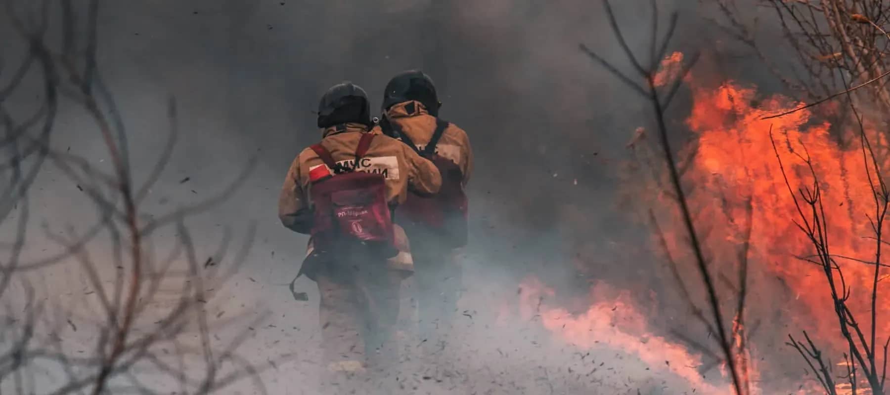 Impact investing and climate risk, a firefighter walking towards a wildfire through smoke.