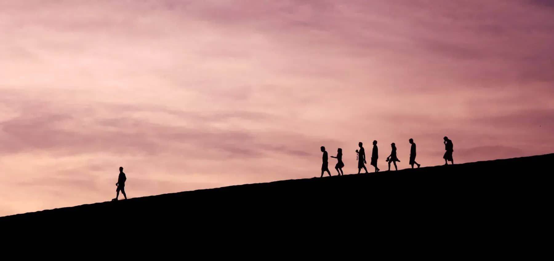 Family wealth transition, silhouettes walking along a ridge beneath a pink dusk sky.