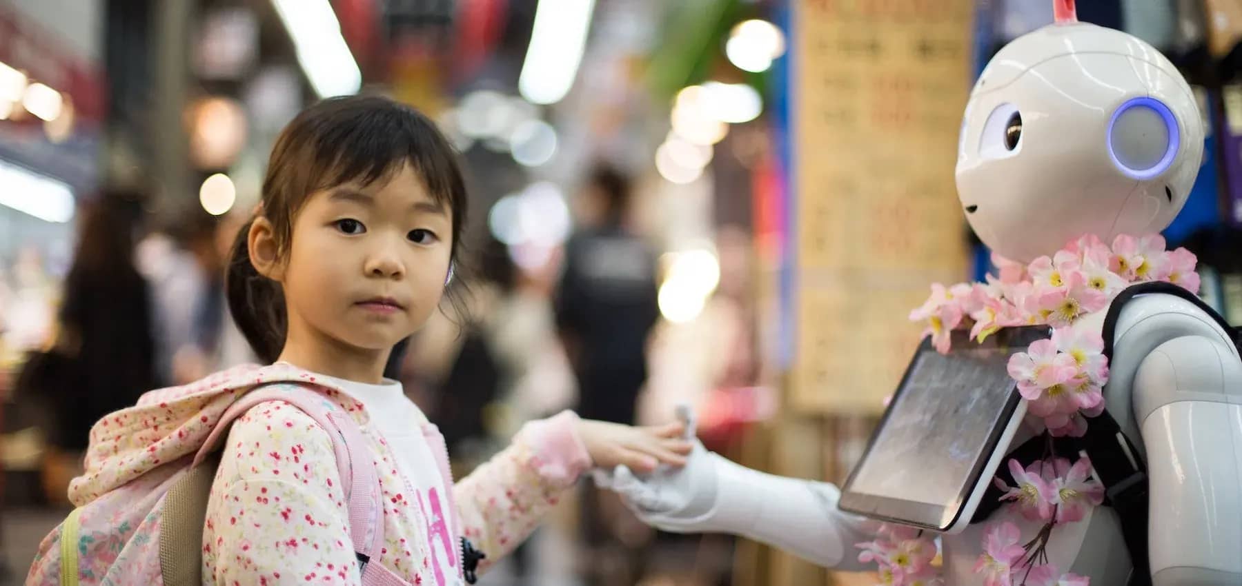 Family business in the digital age, a young girl in a busy lit expo hall with a robot and blossom behind her.