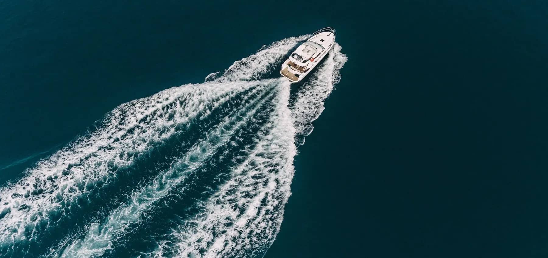 Luxury asset management, an aerial view of a boat carving a white wake through deep blue water.