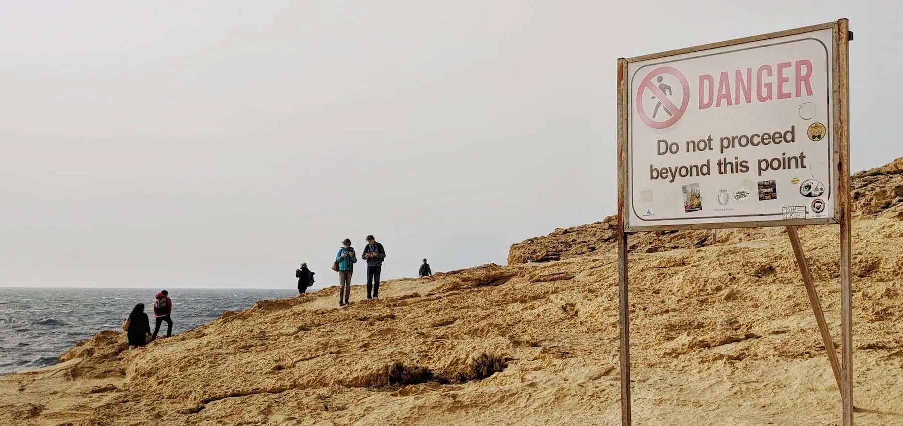 Family office risk, a clifftop warning sign reading do not proceed beyond this point, with people near the edge.
