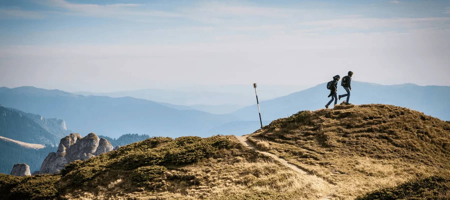 Venture capital communication, two hikers on a ridge above layered blue mountains.