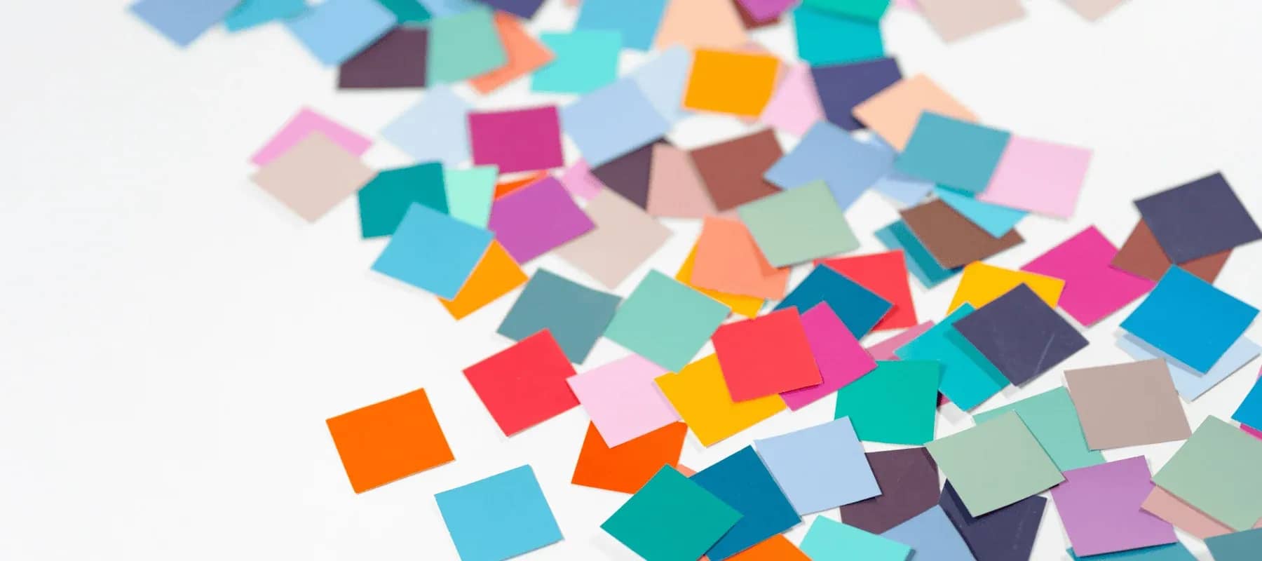 Delegating and outsourcing, scattered squares of coloured paper falling across a pale surface.