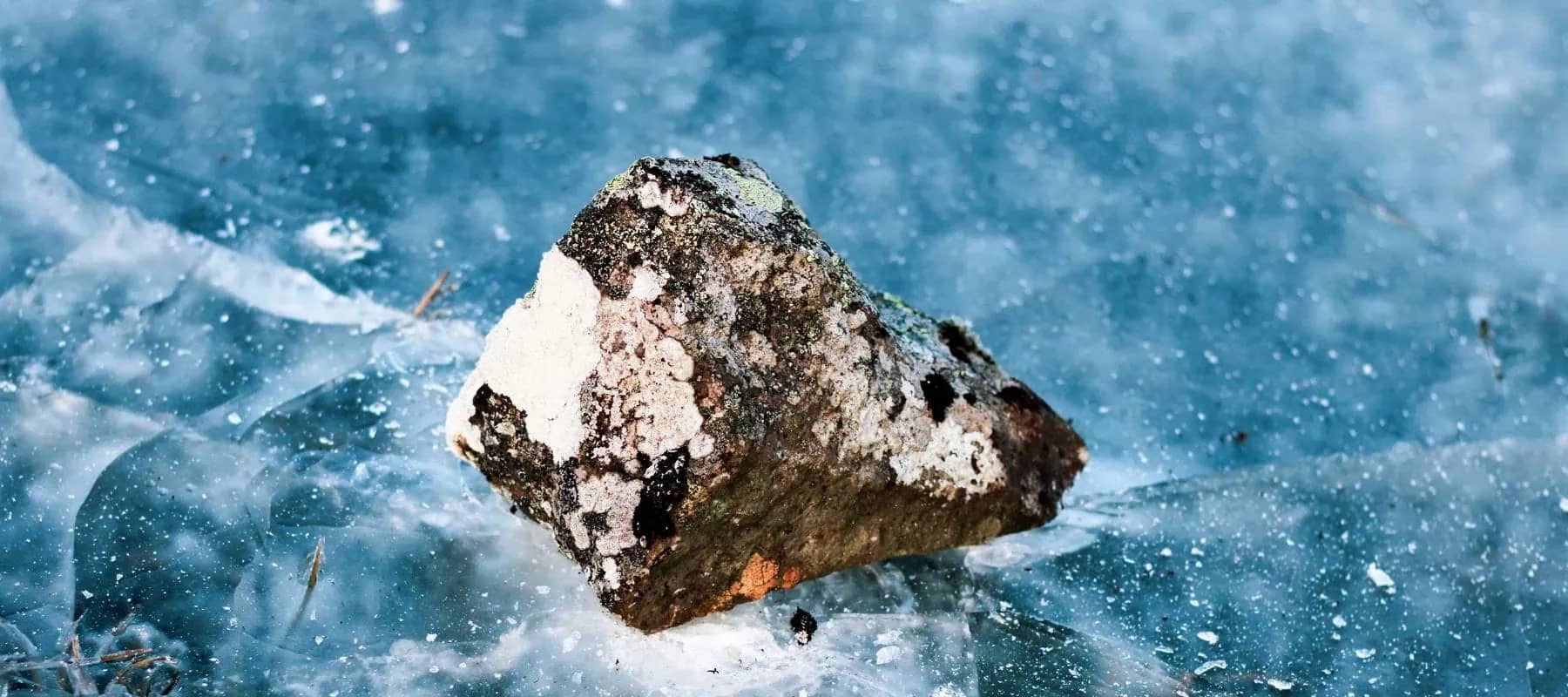Impact optimisation, a dark rock breaking the surface of icy blue water.