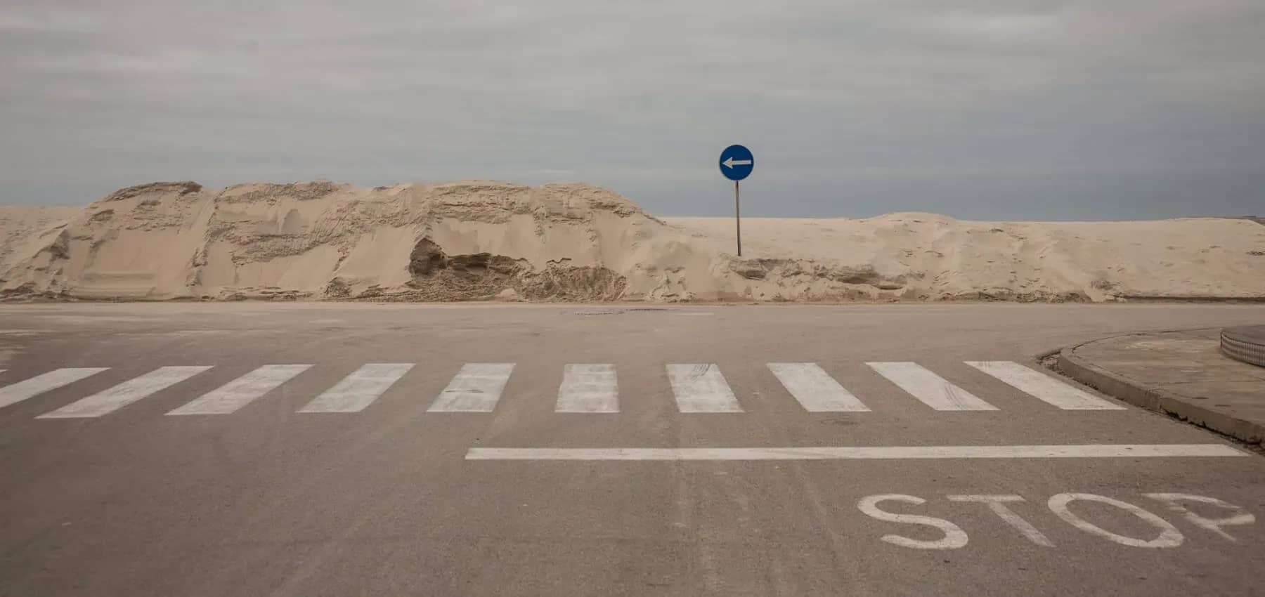 Bitcoin infrastructure investment, a sand dune drifting over a road and zebra crossing.
