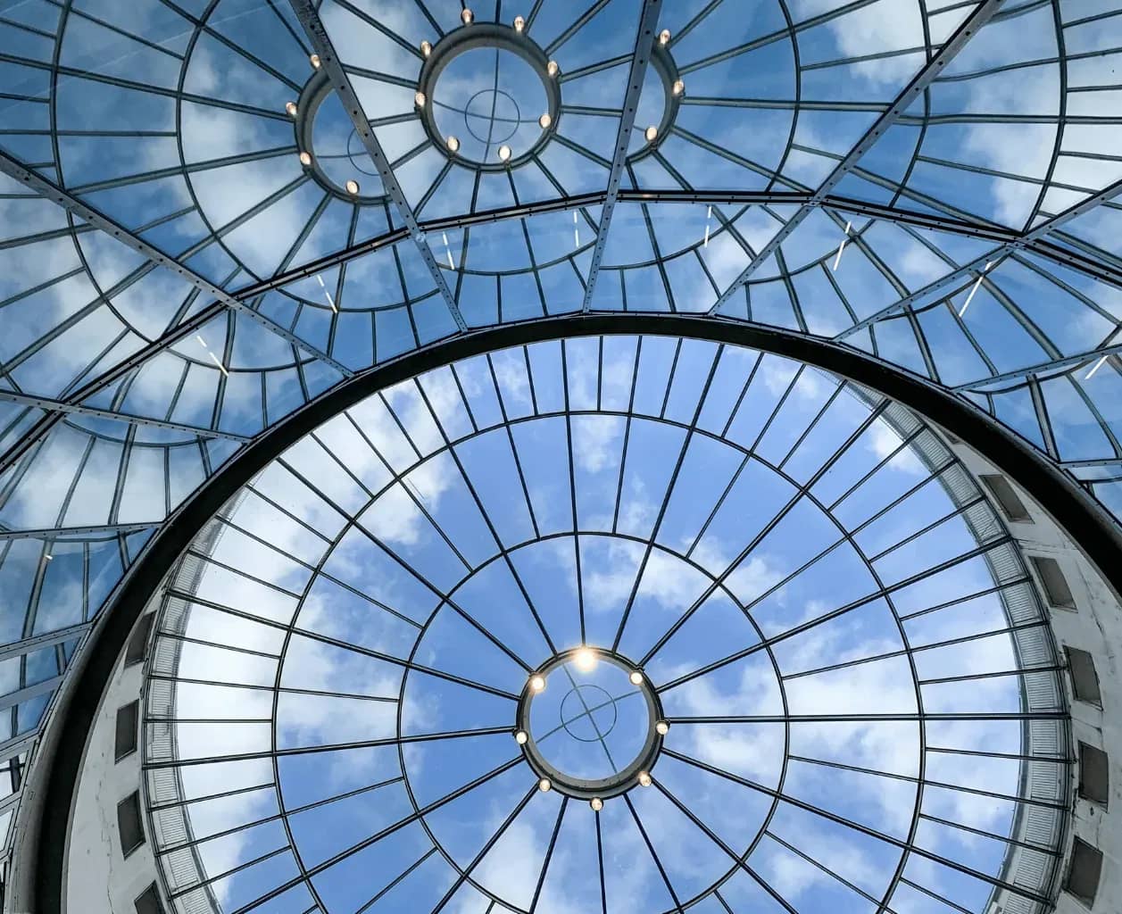 Single-family office infrastructure, a glass and steel domed atrium roof seen from below against a blue sky.