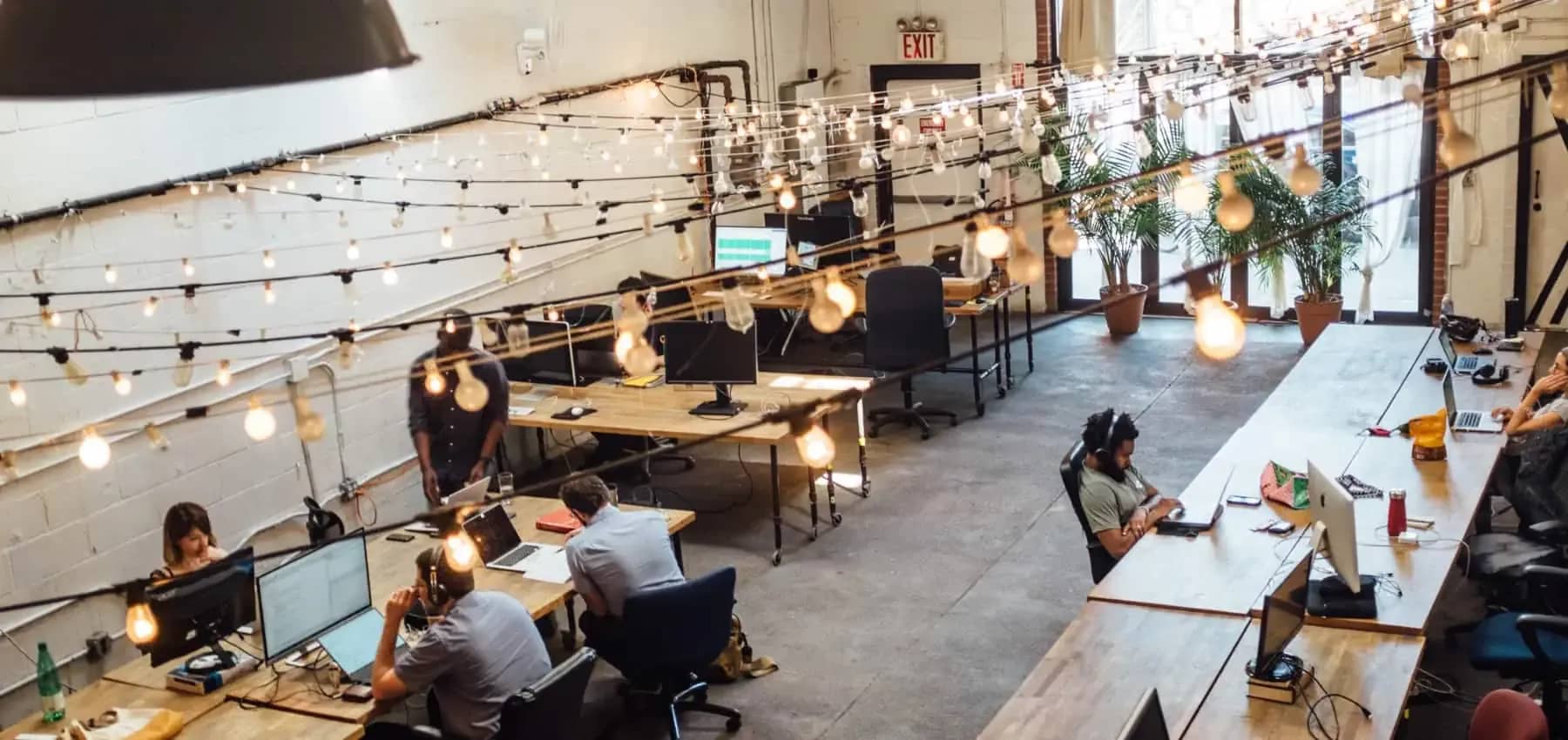 Multi-family office origins, a bright open-plan workspace lit by hanging bulbs.