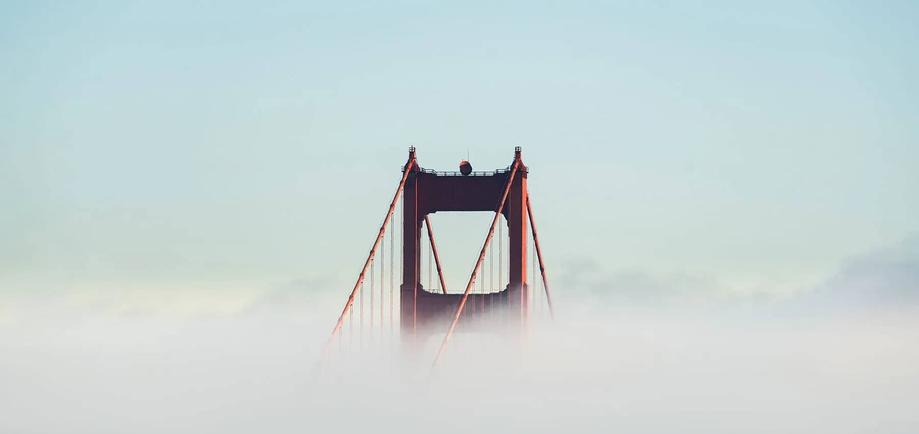 Venture capital in an impact portfolio, a suspension bridge tower rising above low fog.