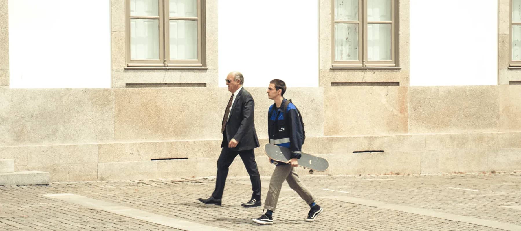 Family offices and venture capital across generations, an older man in a suit walking beside a young man carrying a skateboard.