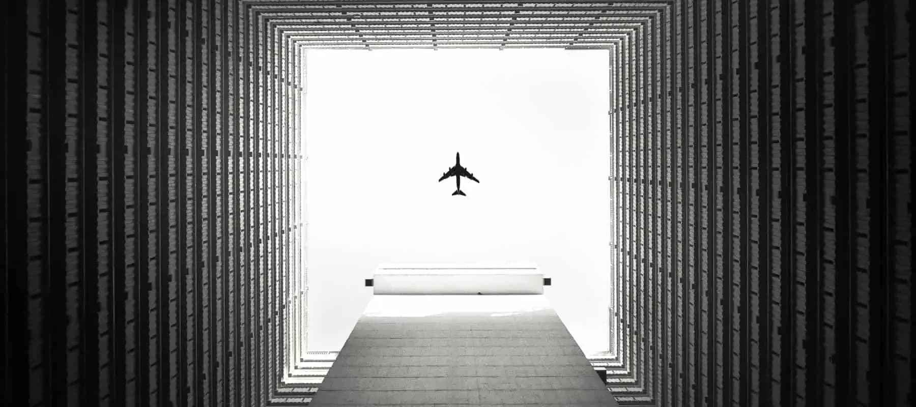 Direct investing, an aeroplane passing between two tall towers against a white sky.