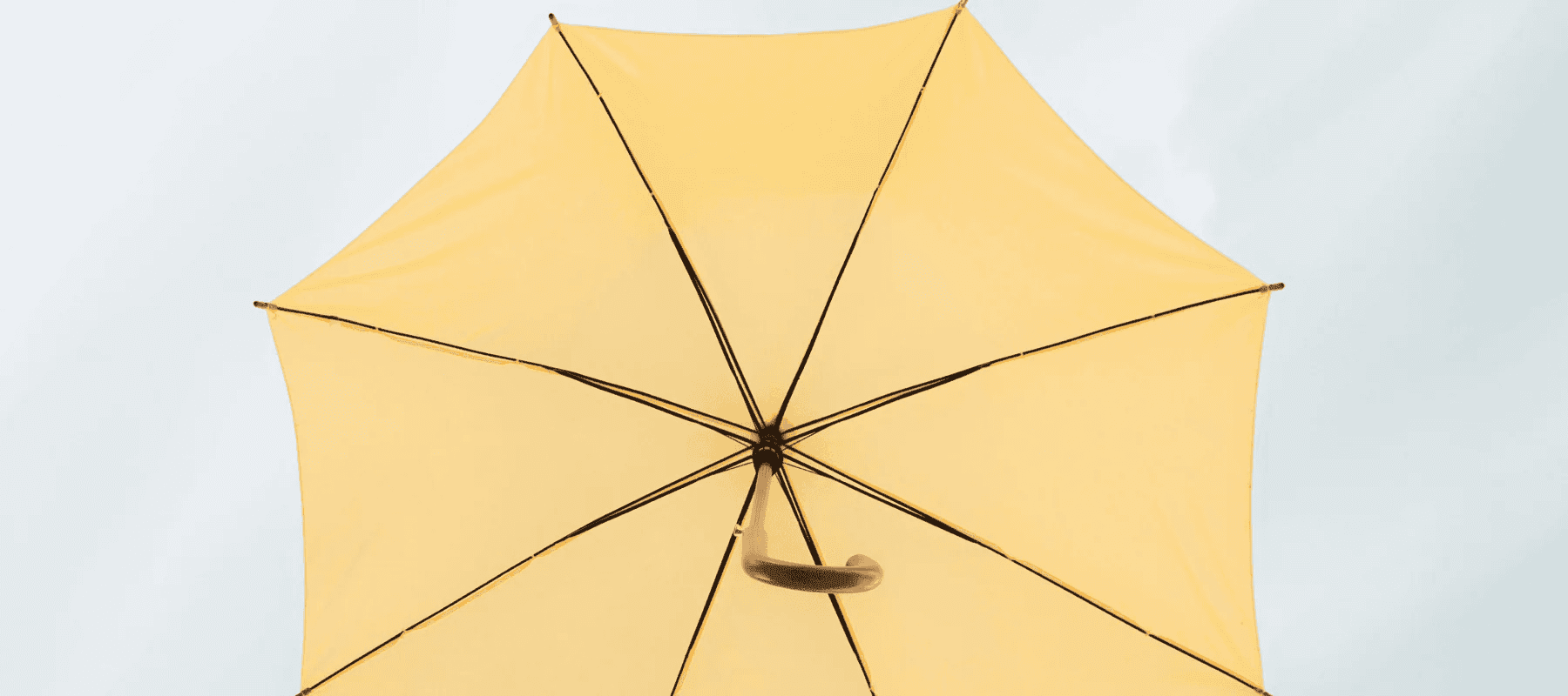 A low-angle view of a bright yellow umbrella against a pale sky, representing an integrated layer of AI for family office software.