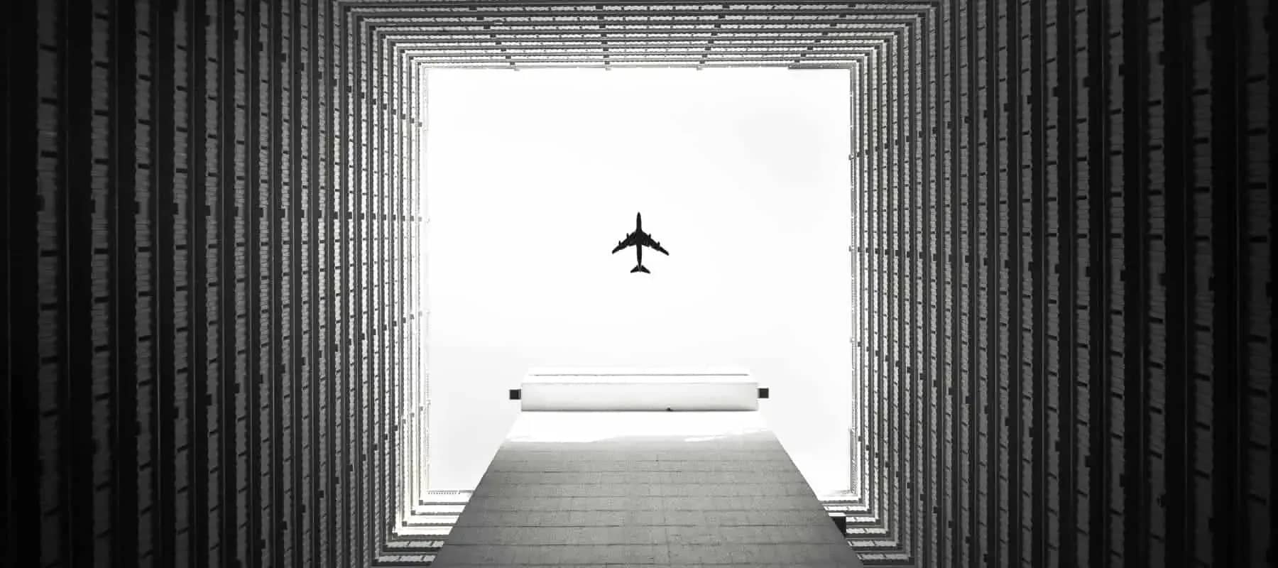 Direct investing, an aeroplane passing between two tall towers against a white sky.