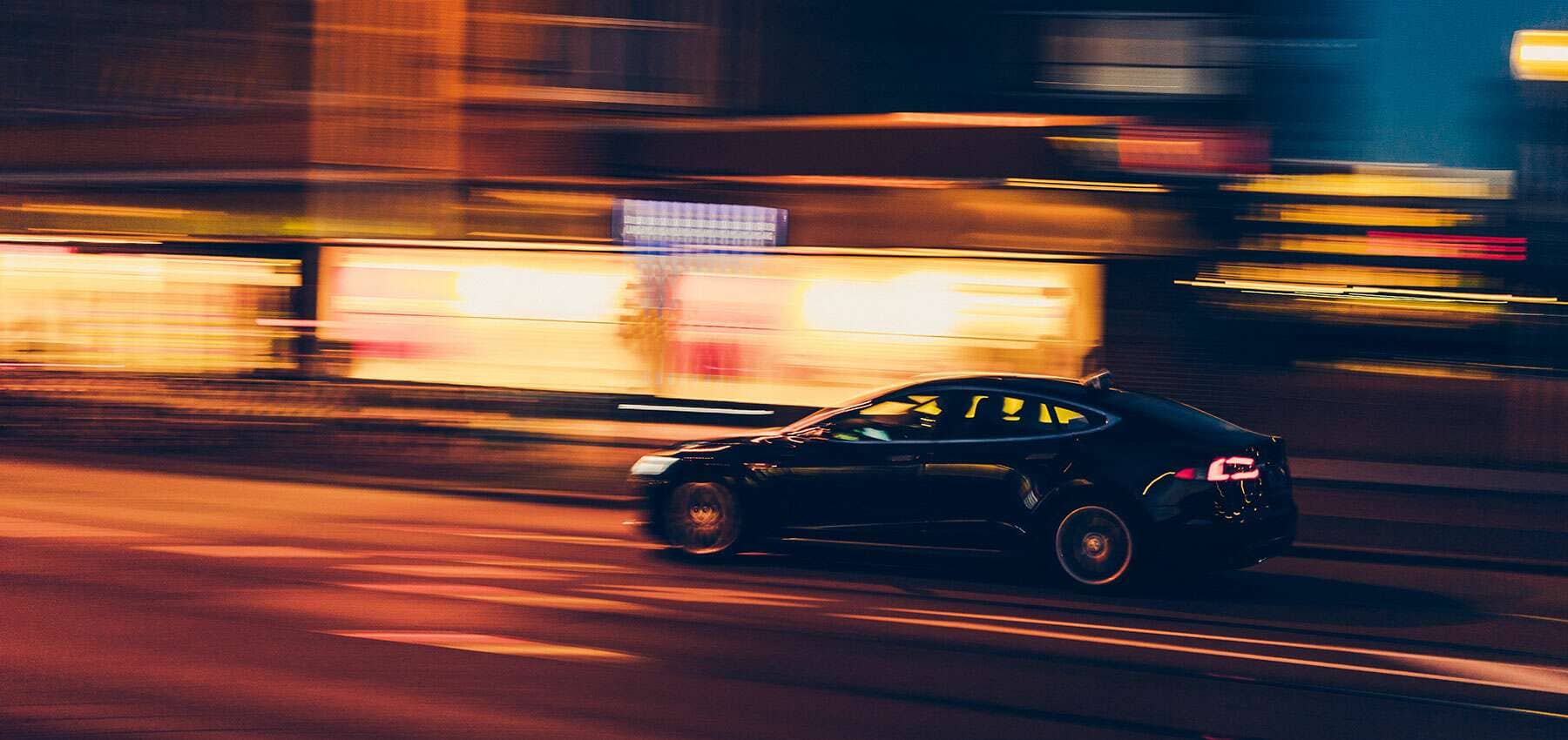 Electric vehicle investment, a dark car blurred at speed past streaks of golden light.