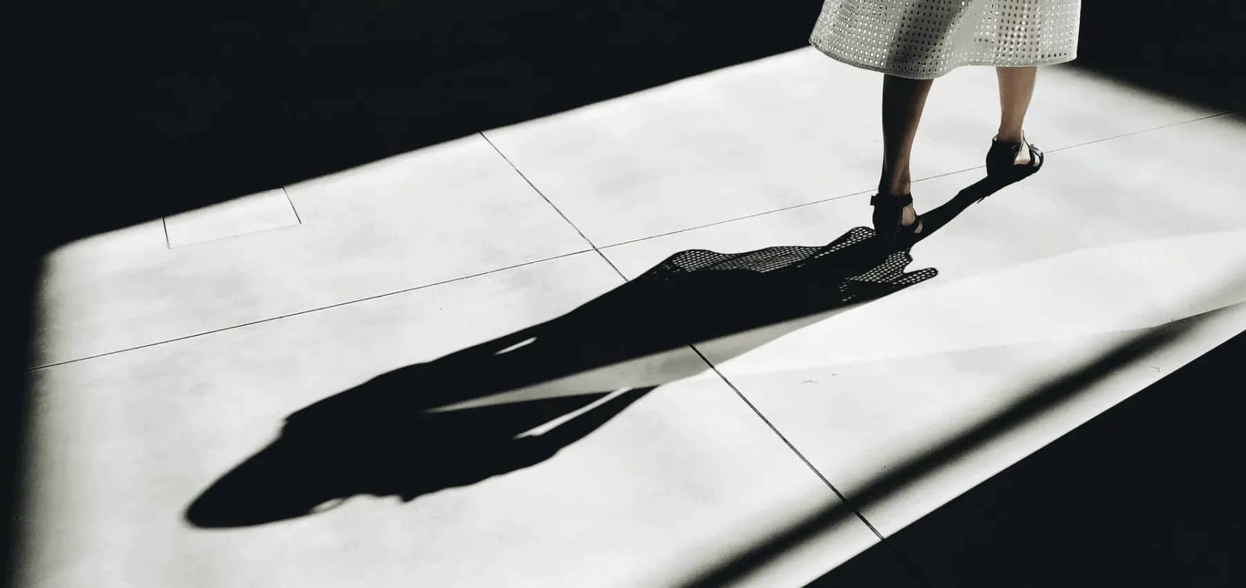 Family business succession, a woman in heels walking across white paving, her long shadow thrown across the stone.