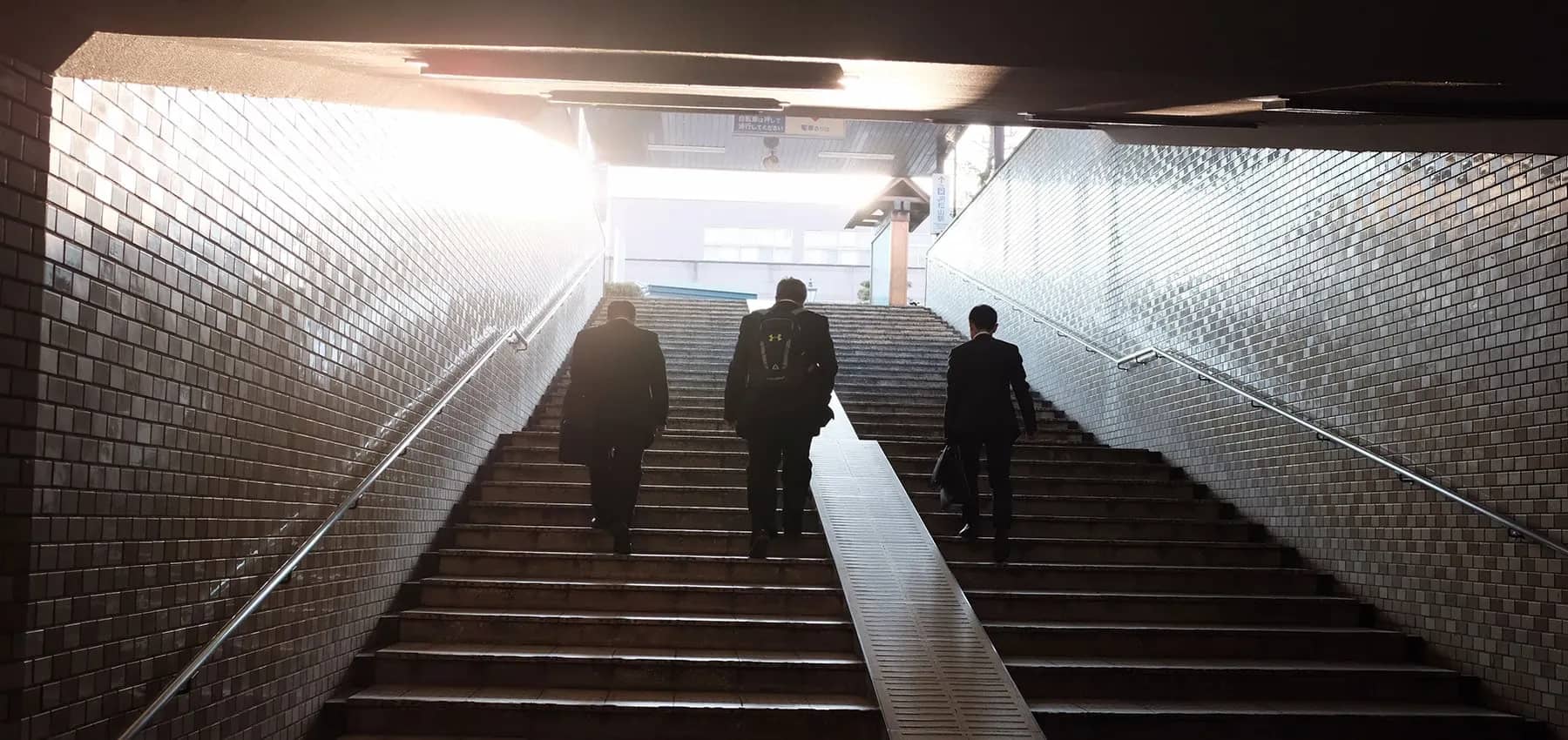 Family office venture capital partnerships, three people in suits climbing a tiled subway staircase towards daylight.