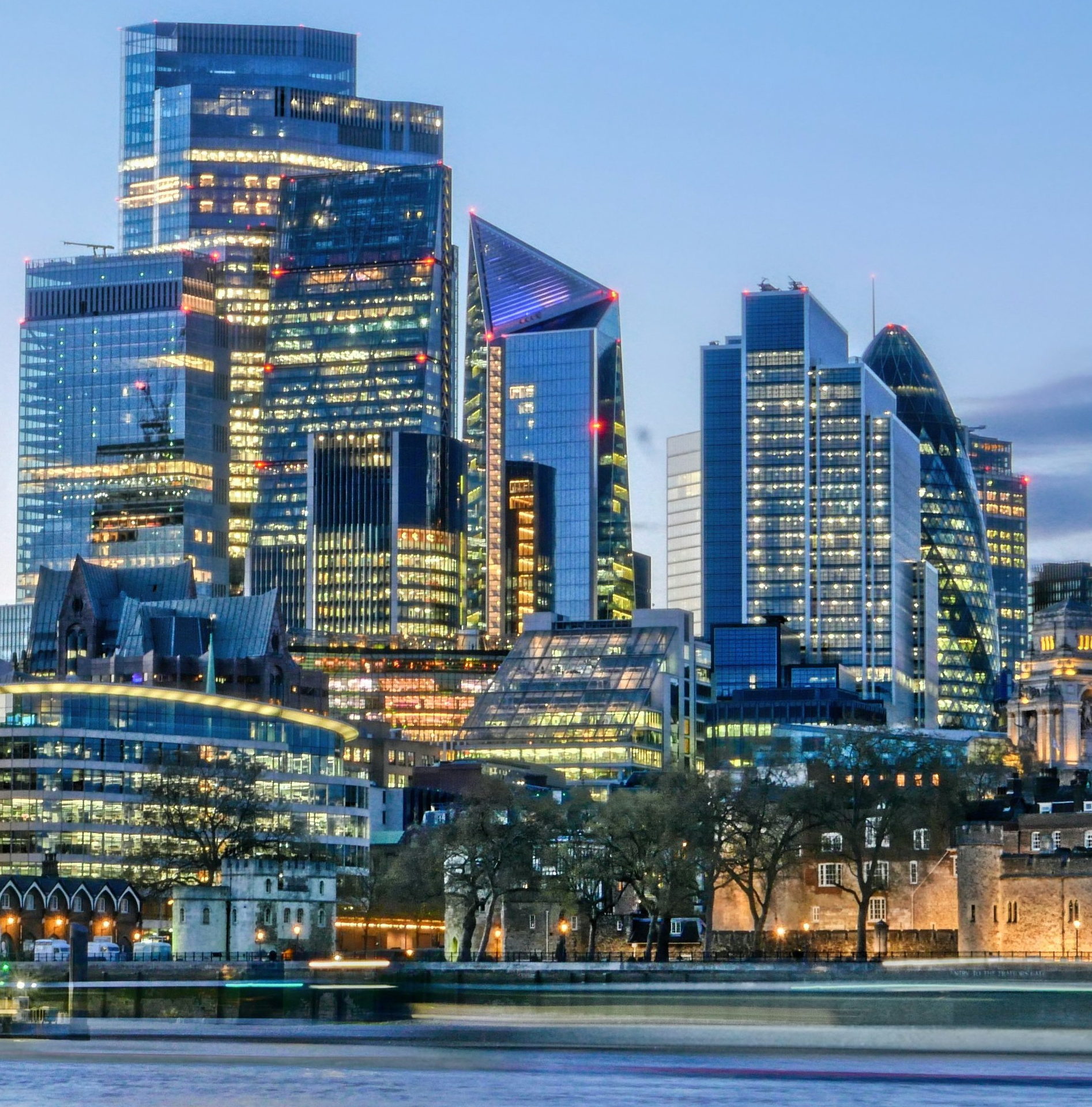 London financial district skyline at dusk with illuminated skyscrapers and River Thames in the foreground